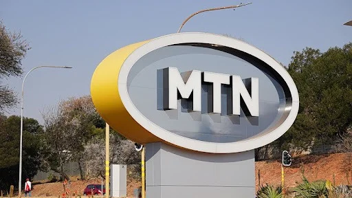 Large outdoor 3D signage of the MTN logo featuring white block letters inside a yellow-rimmed oval.