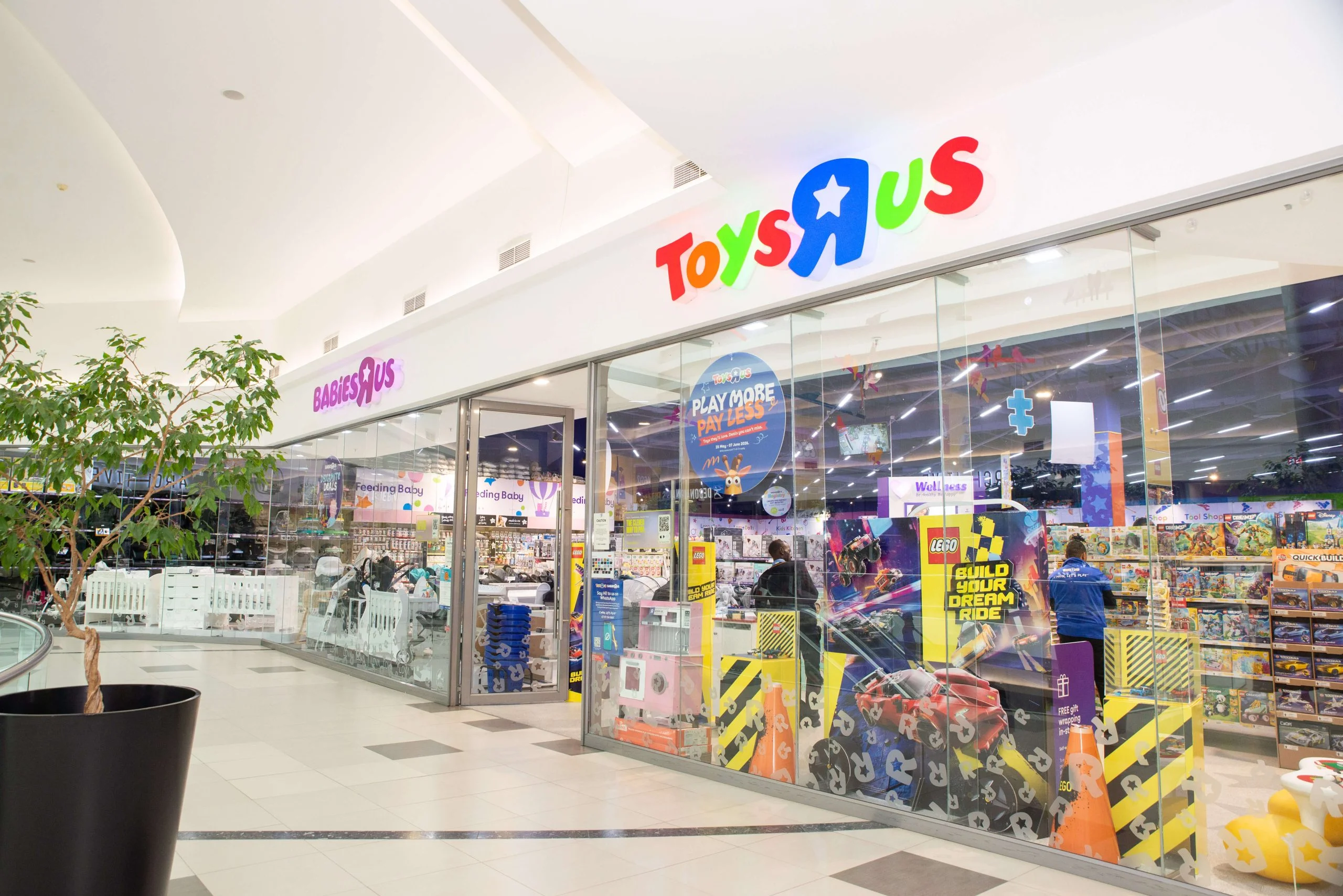 A wide view of a Toys "R" Us storefront inside a modern shopping mall, featuring glass walls, colorful signage, and a neighboring Babies "R" Us section